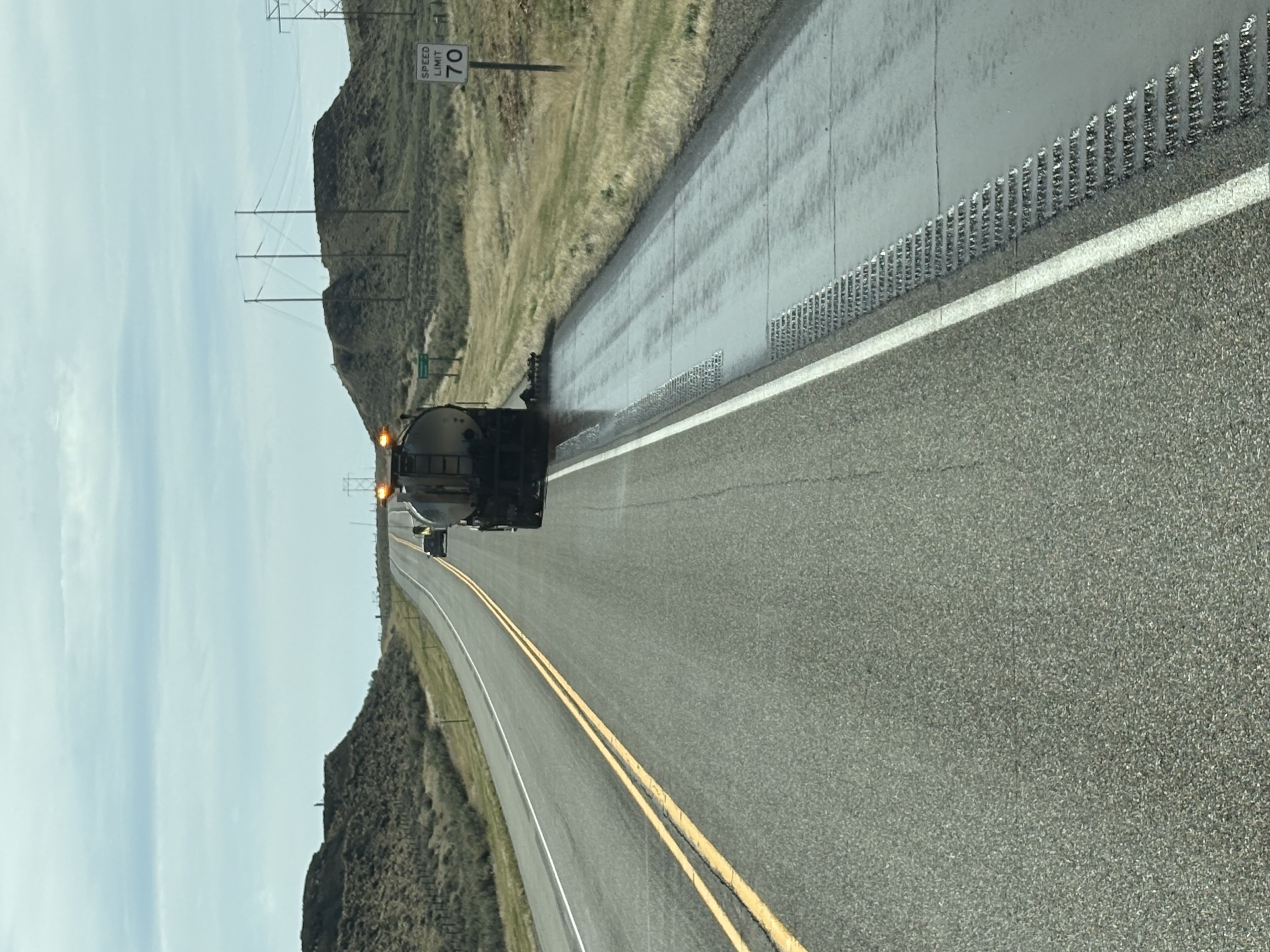 A photo of a WYDOT truck conducting fog sealing work on the shoulder of a highway